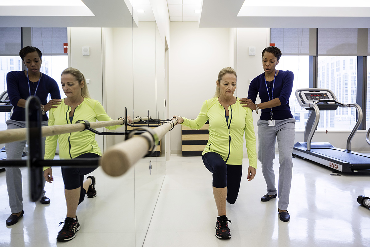 Специалист по реабилитации центра MSK помогает пациенту проходить физиотерапию в спортивном зале.